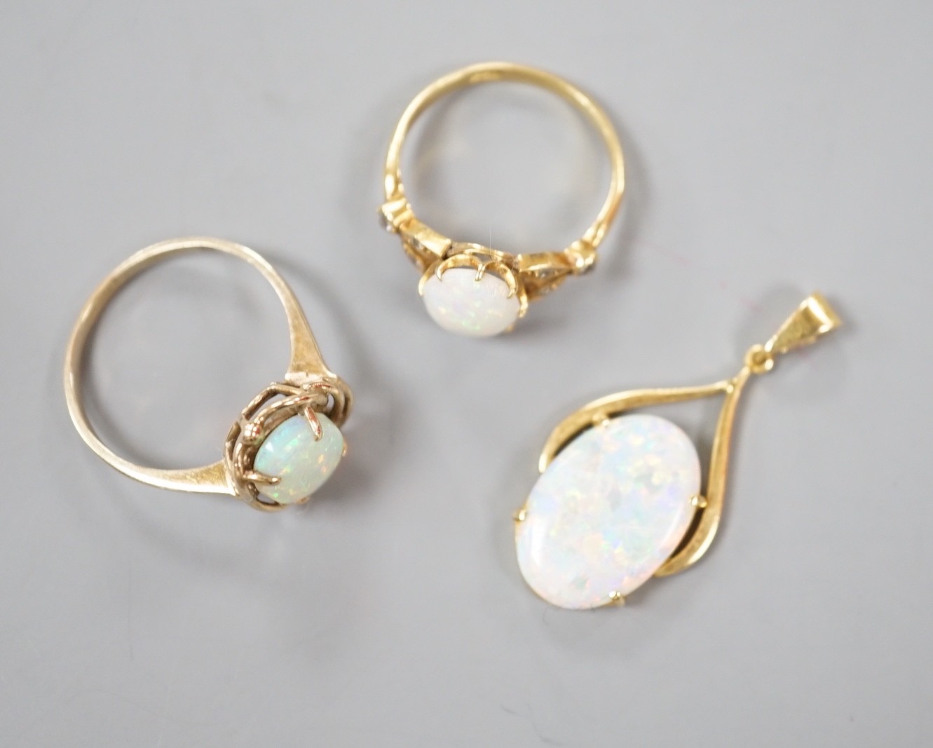 A 9k yellow metal and oval white opal set ring, size O, gross 2.1 grams, an 18ct yellow metal and oval white opal ring, with diamond chip set shoulders and a 70 and white opal set pendant, gross 5.2 grams.